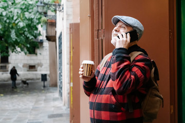 Senior man on the phone with coffee to go and backpack in the city, Barcelona, Spain