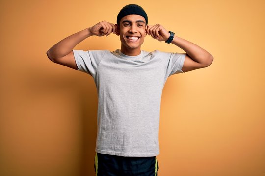Handsome african american sportsman doing sport wearing sportswear over yellow background Smiling pulling ears with fingers, funny gesture. Audition problem