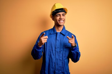 Young handsome african american worker man wearing blue uniform and security helmet pointing...