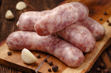 Raw homemade sausages with garlic cloves and spices on wooden table.
