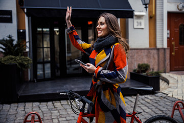 Friendly lady with smartphone waving to someone in the street