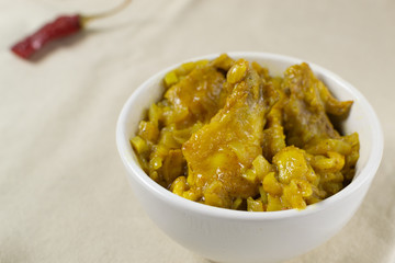 Chicken with curry in a cream bowl on a white background. A traditional dish of Indian cuisine. Close up.