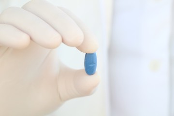 Hand in surgical glove holding a pill