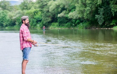 Fototapeta na wymiar Fun of fishing is catching. Fisher with fishing equipment. Fish on hook. Brutal man wear rubber boots stand in river water. Fisher weekend activity. Leisure in wild nature. Fishing masculine hobby