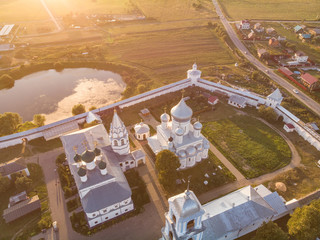 a white Christian church surrounded by houses and a wall with a pond behind the wall in the rays of the setting sun
