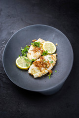 Gebratene Calamari Tuben in Semmelbrösel Panade mit Zitronen Scheiben und Kräuter angeboten als closeup auf einem Modern Design Teller