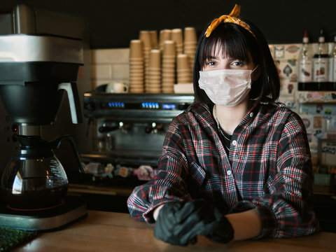 Concept of biohazard security and social responsibility in coronavirus epidemic measures to contain virus spread: young barista girl in medical mask and medical gloves with city cafe background - Powered by Adobe