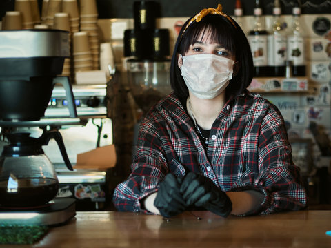 Concept of biohazard security and social responsibility in coronavirus epidemic measures to contain virus spread: young barista girl in medical mask and medical gloves with city cafe background - Powered by Adobe