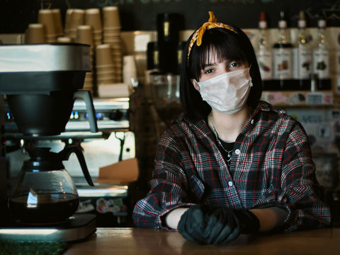 Concept of biohazard security and social responsibility in coronavirus epidemic measures to contain virus spread: young barista girl in medical mask and medical gloves with city cafe background - Powered by Adobe