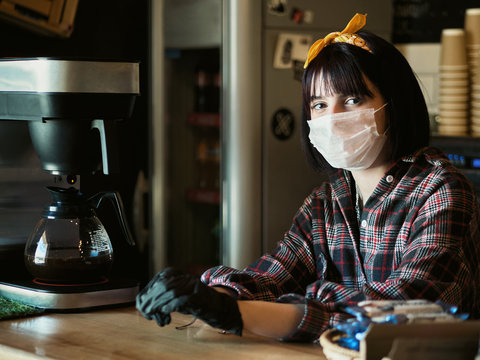 Concept of biohazard security and social responsibility in coronavirus epidemic measures to contain virus spread: young barista girl in medical mask and medical gloves with city cafe background - Powered by Adobe