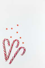 Christmas composition three caramel candy canes, confetti stars on white background with copy space. Festive minimal style flat lay. For greeting card, invitation. Vertical