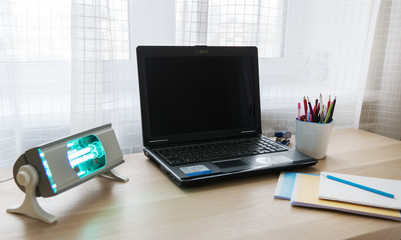 portable quartz ultraviolet lamp for disinfection of home workplace on desk with computer and notebooks on it. healthcare concept, prevention measures from bacteria, coronavirus pandemic