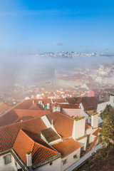 red tile roofs of houses in fog against a blue sky