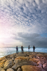 four fishermen on stones against the background of the ocean and sunset sky