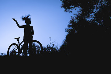Obraz premium silhouette of a young girl with a bicycle at sunset in the middle of nature