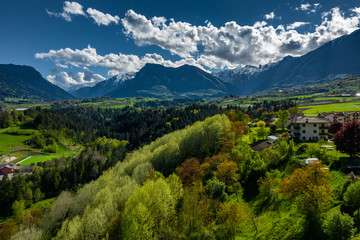 Aerial view of valley Cares, Trentino, green slopes of the mountains of Italy, huge clouds over a valley, roof tops of houses, Dolomites on background, bridges, river and roads, spring colors