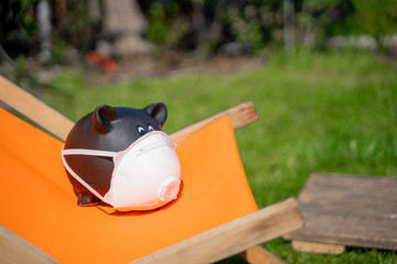 Corona Virus Sparschwein auf einem Liegestuhl. Sommerurlaub Verzicht