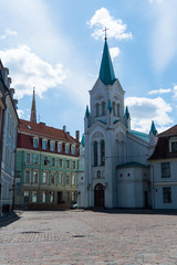 white church with a blue roof and a green house in the square under a blue sky