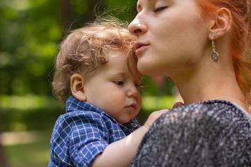 Young red-haired woman with a child. Mom with her son outdoors. Happy family. Young mother. Cute child.