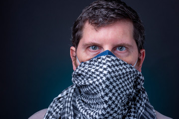 Checker motive scarf over a dark blue N95 respirator face mask on caucasian male. Studio low key profile of man with wide open eyes and bewildered look against a dark grey background