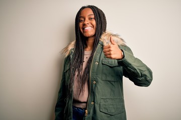 Young african american woman wearing winter parka coat over isolated background doing happy thumbs up gesture with hand. Approving expression looking at the camera showing success.