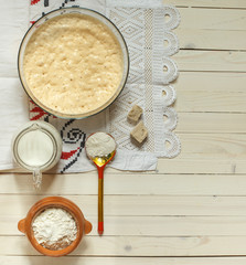 sourdough dough in a bowl, flour and milk on a light wooden background, top view