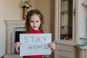 Stay at home concept. Small girl in red T-shirt holding sign saying stay at home for virus protection and take care of their health from COVID-19. Quarantine concept.