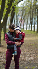 Mom holds a tired little boy in her arms in the park