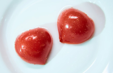 Cherry tomato cut into two parts. Red tomato in the shape of a heart lies on a white plate.
