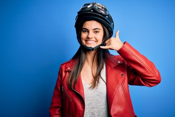 Young beautiful brunette motorcycliste woman wearing motorcycle helmet and jacket smiling doing phone gesture with hand and fingers like talking on the telephone. Communicating concepts.