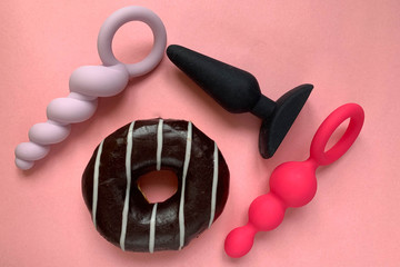 Sex toys. Three butt plags and donut. Pink background. Sex shop assortment - obrazy, fototapety, plakaty