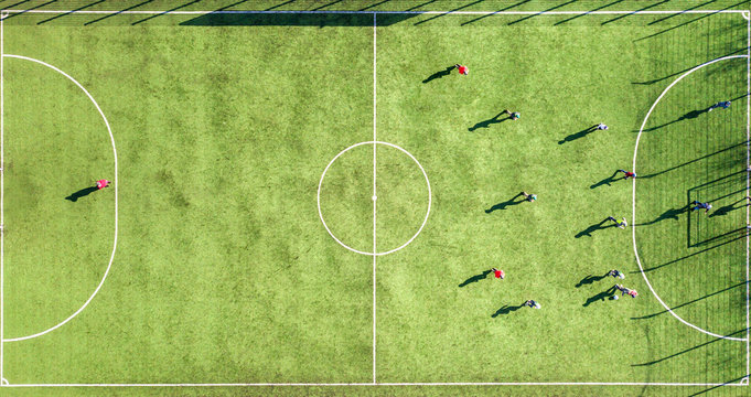 Top down aerial view of green football sports field and players playing football. Drone taken image of small unrecognizable sportsmen on grass covered stadium during sport activities.