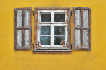 Window frame with shutters in yellow facade.