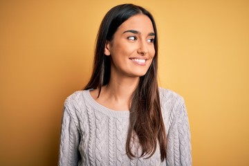 Young beautiful brunette woman wearing white casual sweater over yellow background looking away to...
