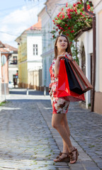 Young woman with shopping bags walking in a small cobblestone street in a city.