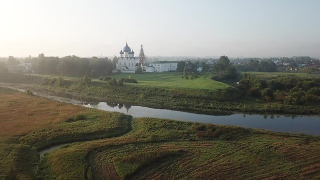 4K aerial dense sunny summer morning video of Suzdal churches, buildings, hills, fields and cathedrals located on Kamenka River shore in Vladimir Region, Russia