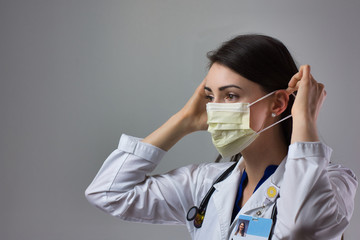 Woman healthcare professional demonstrating proper donning of mask for protection from coronavirus. Up close female healthcare worker putting on safety equipment on grey background