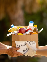 Hand in gloves give food donation box to hands of a senior beggar during coronavirus pandemic...