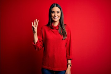 Young beautiful brunette woman wearing casual sweater over isolated red background showing and pointing up with fingers number four while smiling confident and happy.