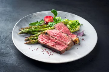 Poster Barbecue dry aged wagyu entrecote beef steak with lettuce and green asparagus as closeup on a modern design plate © HLPhoto