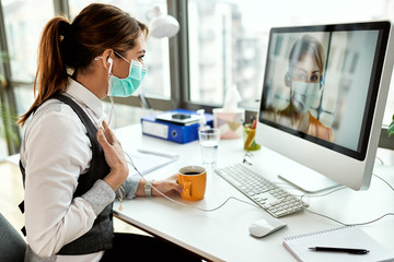 Businesswoman with face mask having video chat with her colleague in the office.