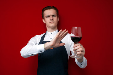 professional sommelier with a glass of red bad wine refuses to drink on a red background, the guy the waiter does not recommend drinking alcohol