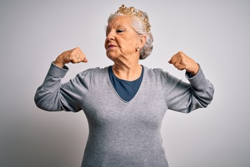Senior beautiful grey-haired woman wearing golden queen crown over white background showing arms muscles smiling proud. Fitness concept. © Krakenimages.com