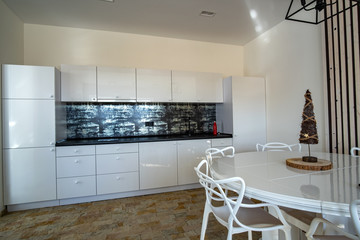 Interior of modern spacious kitchen with white walls, decorative wooden elements, contemporary furniture and big soft couch.