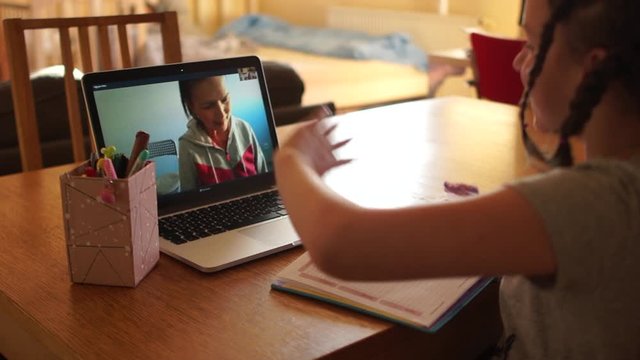 Schoolgirl with pigtails talking to her teacher on Skype, waving hands to each other. Quarantine during Coronovirus Covid-19. Quarantine and Social distancing concept, distance learning