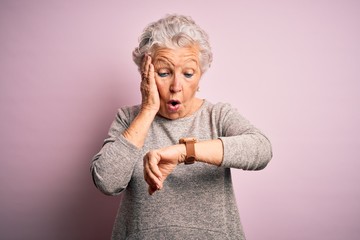 Senior beautiful woman wearing casual t-shirt standing over isolated pink background Looking at the watch time worried, afraid of getting late
