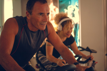 People doing spinning with electric bikes in a gym while one of them is listening to music