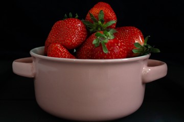 Fresh red strawberries in a bowl. Strawberry fruits on a black background. Copy space for text. Concept banner or panorama. Top view.