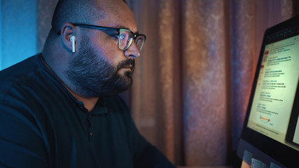 Distant work, man in glasses working at computer at night, freelancer at home.