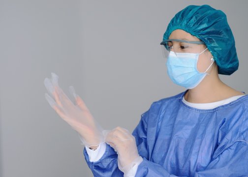 m&eacute;dico mujer que se pone guantes de l&aacute;tex y usa tapabocas o mascara facial y lentes de seguridad para atender pacientes infectados